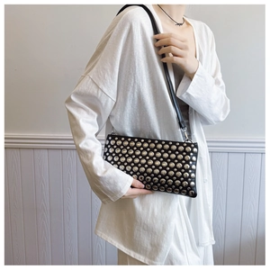 Detail of a black synthetic leather bag with silver round rivets and slim shoulder strap