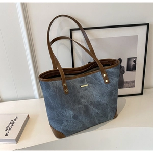 Detail view of large tote bag with blue-grey textured surface and brown leather handles