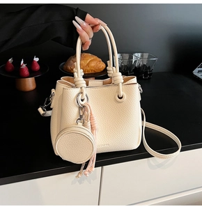 Detail of cream white bucket bag with knotted handle and round coin purse charm