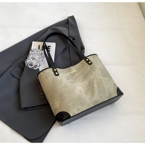 Close-up of grey-green tote bag with gold metal trim and black handles on desk