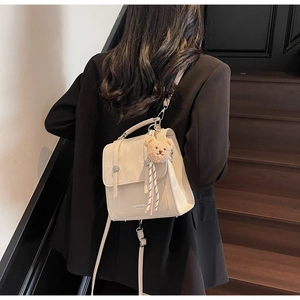Dettaglio di zaino in pelle PU beige con trama scamosciata e ciondolo orsetto marrone
