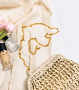Detail of light beige woven summer bag with delicate gold chain strap on soft fabric