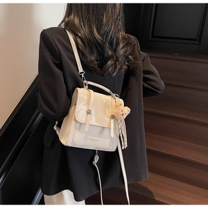 Borsa a tracolla beige su blazer nero con ciondolo a forma di orsetto e nastro