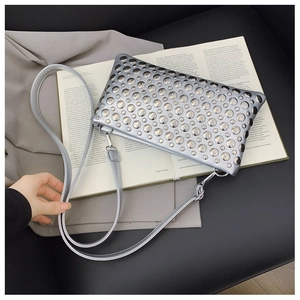 Detail of silver rectangle envelope bag with metallic studs and a leather strap on a book