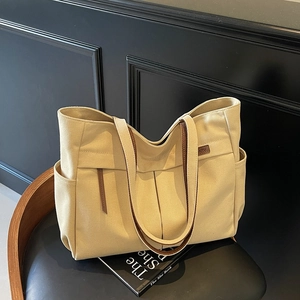 Minimalist canvas tote bag with brown leather handles and large capacity on a black chair