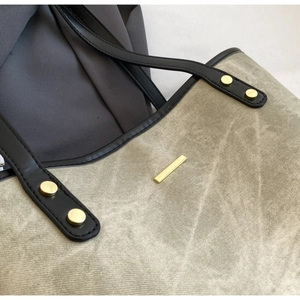 Detail of gray-green canvas tote bag featuring golden metal trim and black leather straps