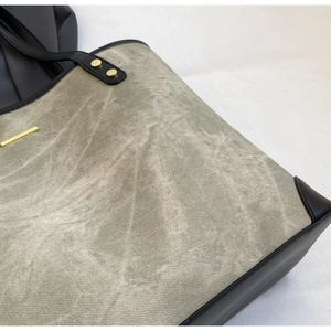 Detail shot of green tote bag with black accents and gold hardware rivet textures