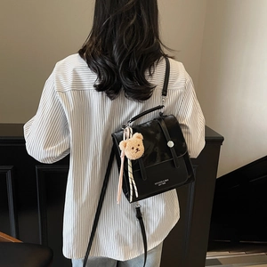 Versatile borsa a tracolla squadrata in pelle nera con manico e ciondolo a forma di orsetto