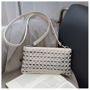 Close-up of white leather shoulder bag featuring silver rivet studs on a grey blazer