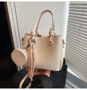 Detail of cream bucket bag with lychee texture leather, knot handle and round pouch charm