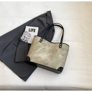 Detail view of large grey tote bag with black leather trim and gold metallic hardware accents