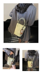 Détail d'un sac seau en cuir verni vert clair avec un pendentif cartoon et une bandoulière