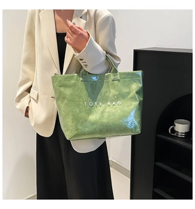 Close-up of metallic green tote bag with wrinkled texture and bold printed white logo