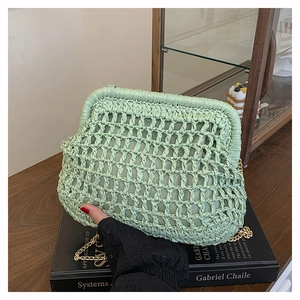 Close-up of a pale green crochet cloud clutch with a gold chain strap on a black book