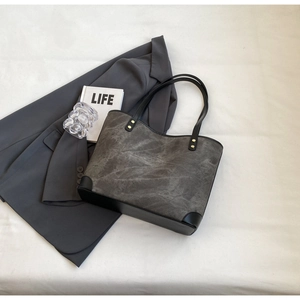 Detailed view of tote bag with grey textured canvas, black leather trim and gold rivets