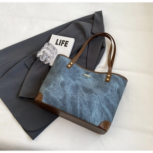 Detail of blue textured tote bag with brown leather trim and golden metal bar accent