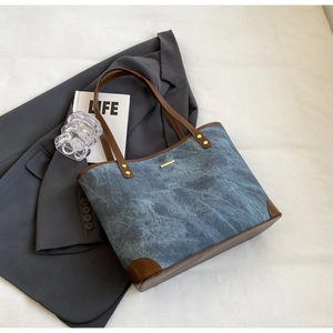 Detail of vintage blue denim tote bag with brown leather trim and metallic accents