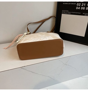 Detailed base view of an off-white textured tote bag with brown leather bottom and tassel
