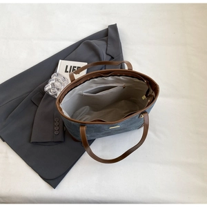 Detail view of large grey tote bag with brown leather handles and gold zipper closure
