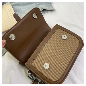 Detail of magnetic snap closures on brown leather and straw patchwork crossbody bag
