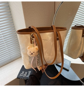 Detail of cream tote bag with brown straps and cute teddy bear charm accessory