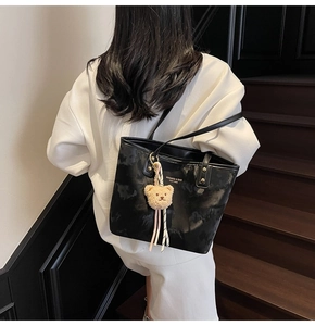 Close-up of black PU leather tote bag featuring golden logo and teddy bear charm