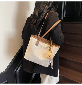Detail of cream tote bag with brown straps and a cute plush bear charm in a stair setting