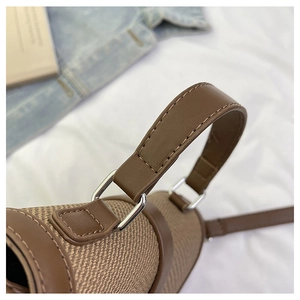 Close-up of brown leather handles and silver D-ring detail on khaki woven handbag