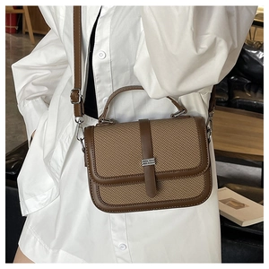 Close-up of brown woven texture crossbody bag with metallic clasp on white shirt background