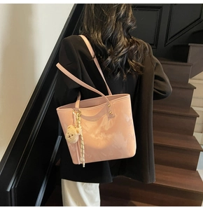 Pink glossy tote bag with teddy bear charm shown on model in a modern staircase setting