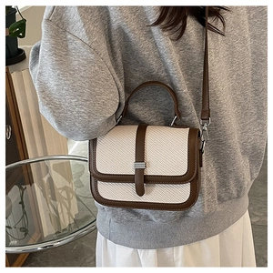 Detail of a woven cream shoulder bag with brown leather trim and metal clasp on a model