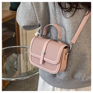 Model wearing a small pink textured crossbody bag with silver buckle and top handle