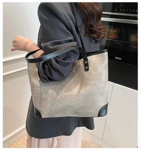 Detail of the gray canvas tote bag with black leather handles and metal snap button clasp