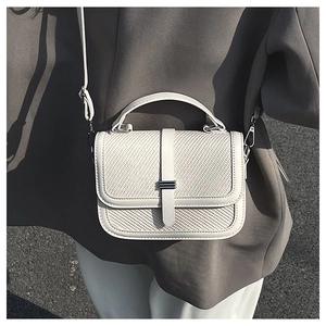 Detail of cream crossbody bag featuring woven texture flap and metallic closure in street style
