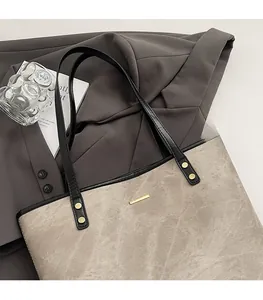 Detail of grey suede tote bag with black leather straps and gold metal logo on blazer