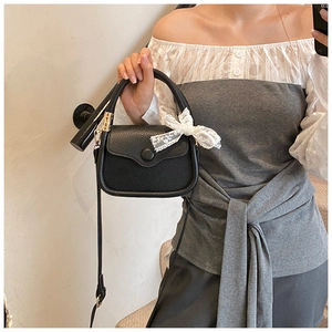 Detail of black pebbled leather handbag with adjustable strap and white lace bow accessory