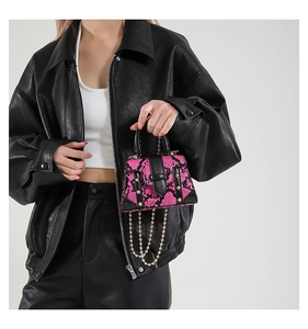 Detail of pink snakeskin mini bag with gold rivets and chain on black leather jacket