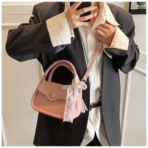 Pink mini tote bag with litchi texture leather and white lace bow detail worn with suit