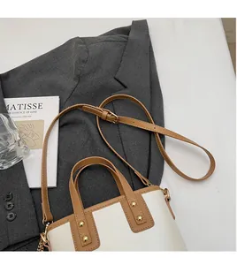 Detail of white and brown contrast leather bucket bag with gold rivets on a white desk