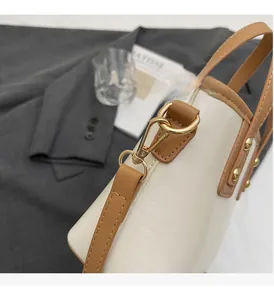 Detail of golden metal clasp and brown leather trim on the cream bucket handbag