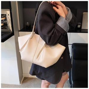 Detailed side view of off-white lychee textured tote bag styled with a dark blazer
