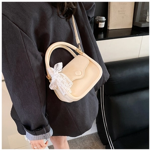 Detail of cream-colored cross-body bag with litchi grain texture and lace bow accessory