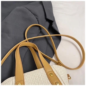 Détail du sac seau tressé blanc avec poignées brunes sur fond de costume gris élégant