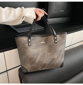 Close-up of gray tote bag with marble texture, black leather trim and gold rivet details