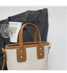 Detail of a contrast color bucket bag with brown handles and gold rivets on a beige surface