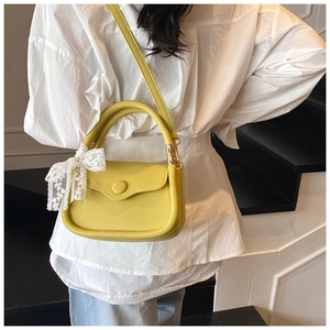 Detailed view of yellow lychee leather handbag with lace bow on modern staircase