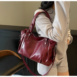Detail of burgundy tote bag with silver rivets and polished leather texture on a model