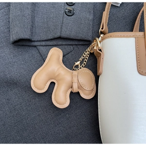 Detail of a camel dog-shaped leather bag charm with gold chain on a tote bag