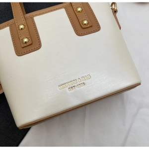 Detail of beige and brown bucket bag showing gold rivets and embossed logo lettering