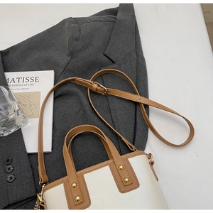 Detail of white leather bucket bag with brown handles and gold hardware on grey suit